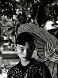 Model Xiaorui Li holding a parasol beneath foliage in a monochrome fashion editorial for Vogue Philippines.