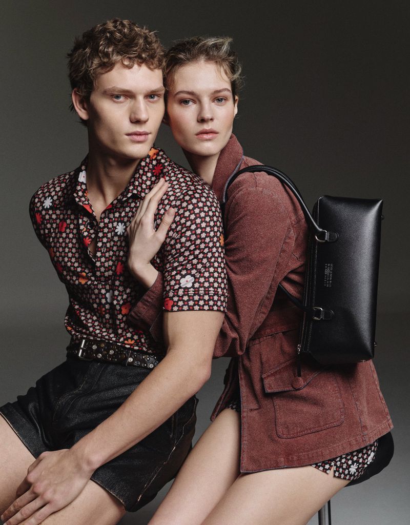 Fashionable couple in a studio portrait. Man in patterned shirt and denim shorts with a woman in a jacket and backpack.