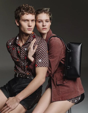 Fashionable couple in a studio portrait. Man in patterned shirt and denim shorts with a woman in a jacket and backpack.