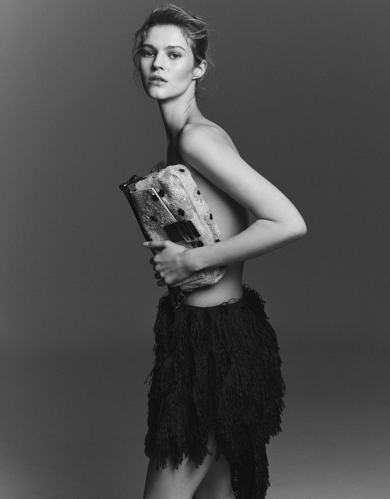 Monochrome fashion portrait of a model holding a textured patterned clutch against a dark gradient background.
