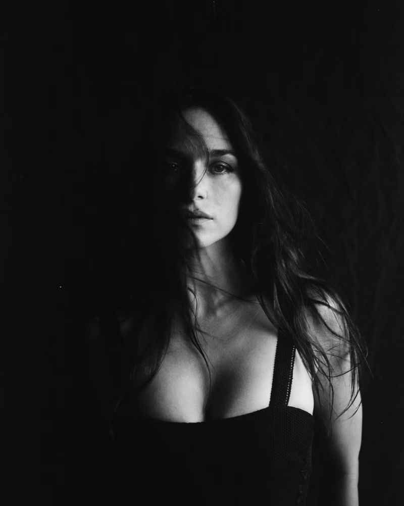 Striking black and white portrait of a woman with long, dark hair. She is facing the camera with serious expression against a dark backdrop.