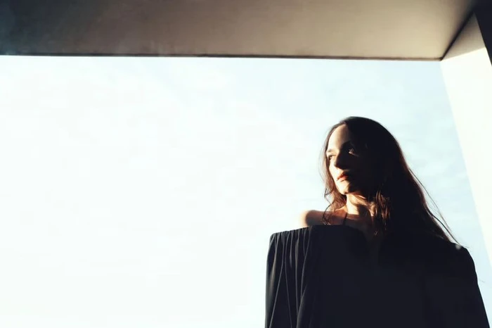 Woman in dark off-the-shoulder top framed against a bright architectural opening with direct sunlight