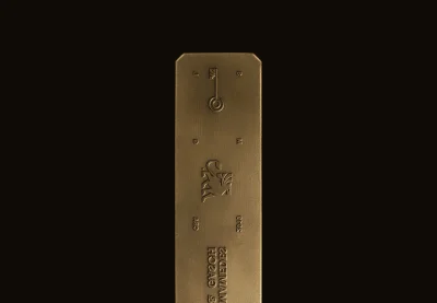 Vertical metallic bronze brand plate featuring embossed logos and text against a dark background