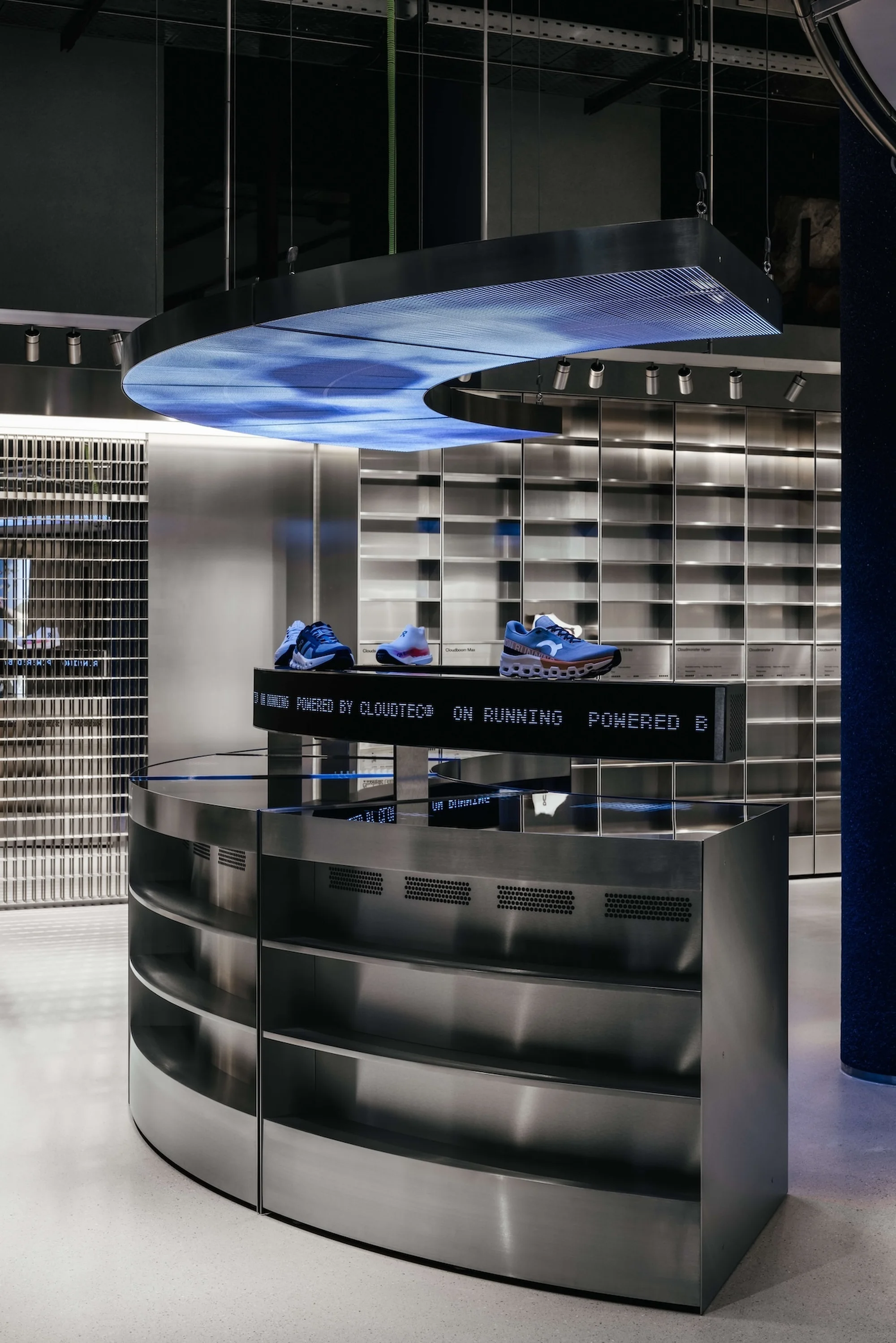 Interior of a modern retail store featuring athletic shoes displayed on a curved metallic stand with a digital display overhead.