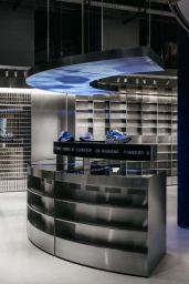 Metallic curved retail display counter with athletic shoes under a suspended digital screen inside a store