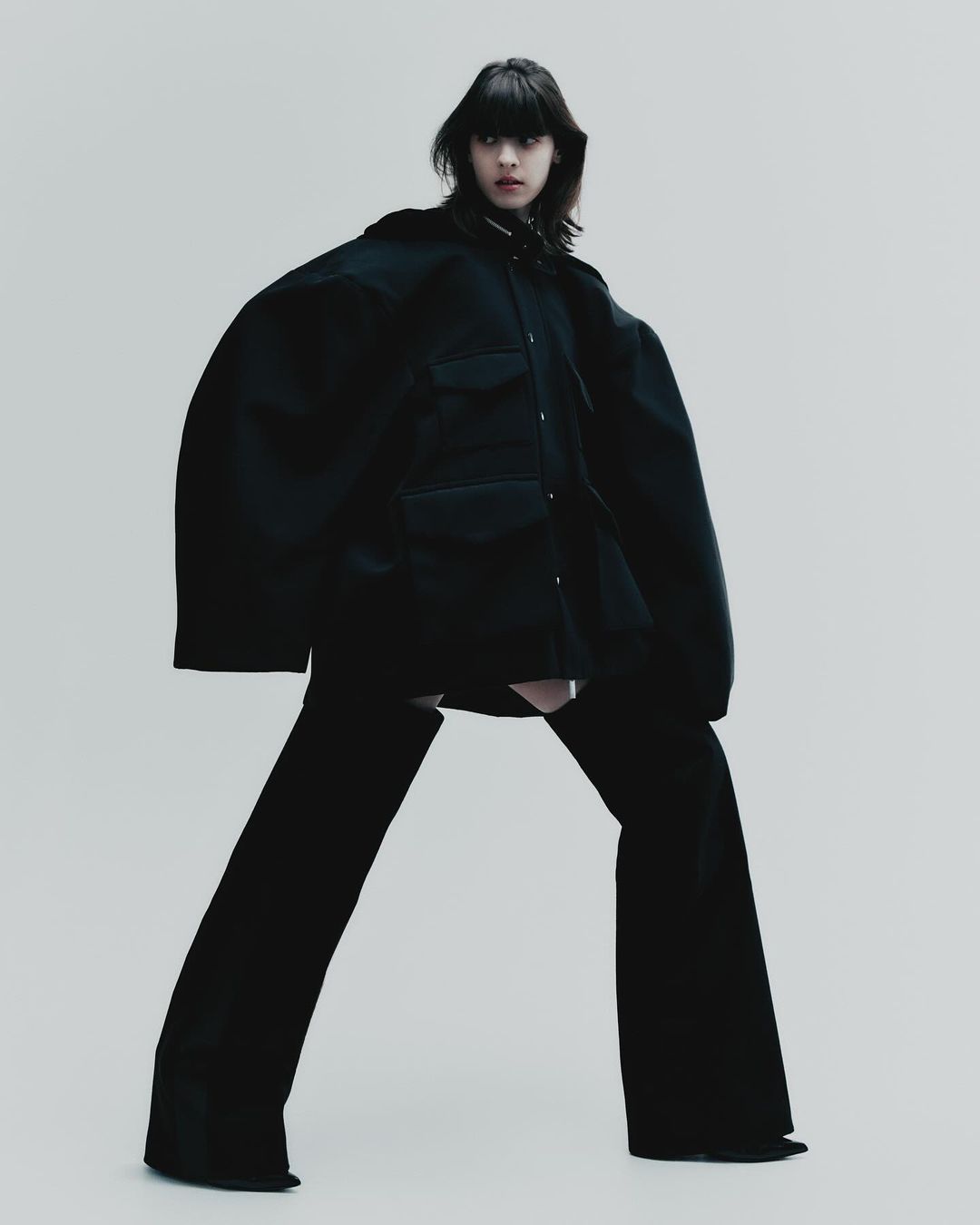 Model in an oversized black jacket and matching trousers against a plain light grey backdrop for Elle Mexico editorial.