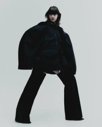 Model in an oversized black jacket and matching trousers against a plain light grey backdrop for Elle Mexico editorial.