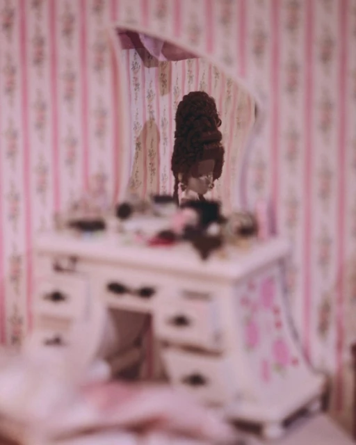 Vintage vanity table with mirror, makeup, and beauty accessories in a boudoir with pink floral wallpaper and shallow depth of field.