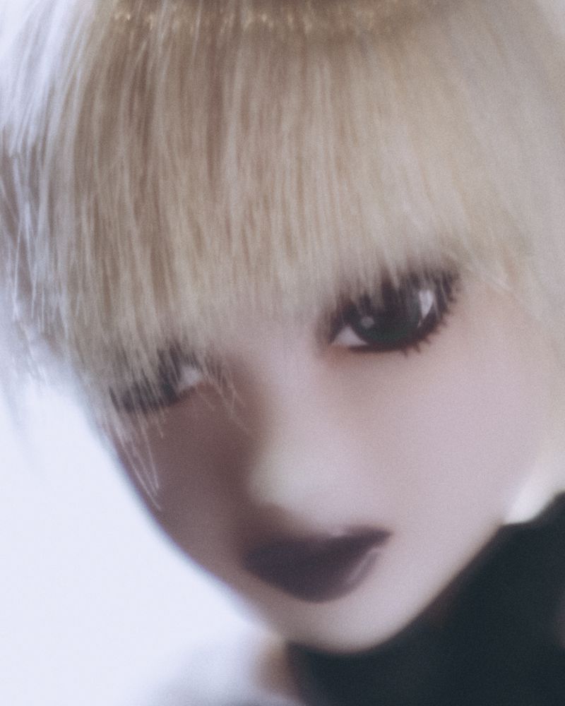 Close-up portrait of a miniature doll with blonde bangs and dark lipstick for Novembre Global.