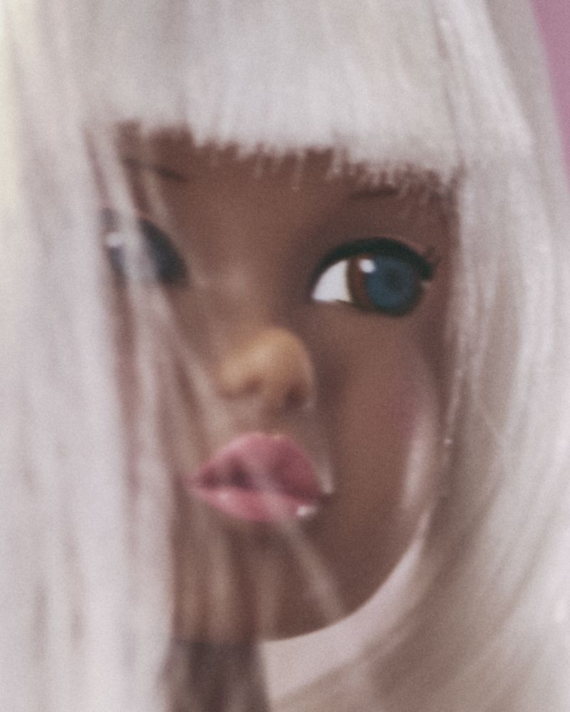Close-up of a Black fashion doll with light pink lips and white hair. The doll's face and white hair are blurred slightly.