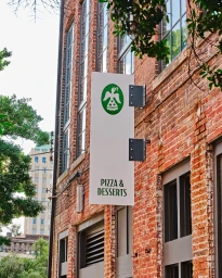 Vertical sign reading Pizza and Desserts mounted on a red brick building exterior