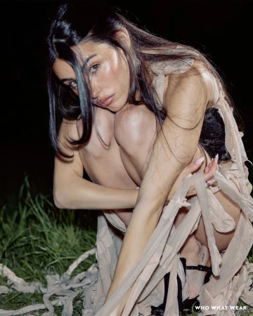 Madison Beer crouching in a sheer beige ruffled dress amidst dark grass at night with direct flash lighting