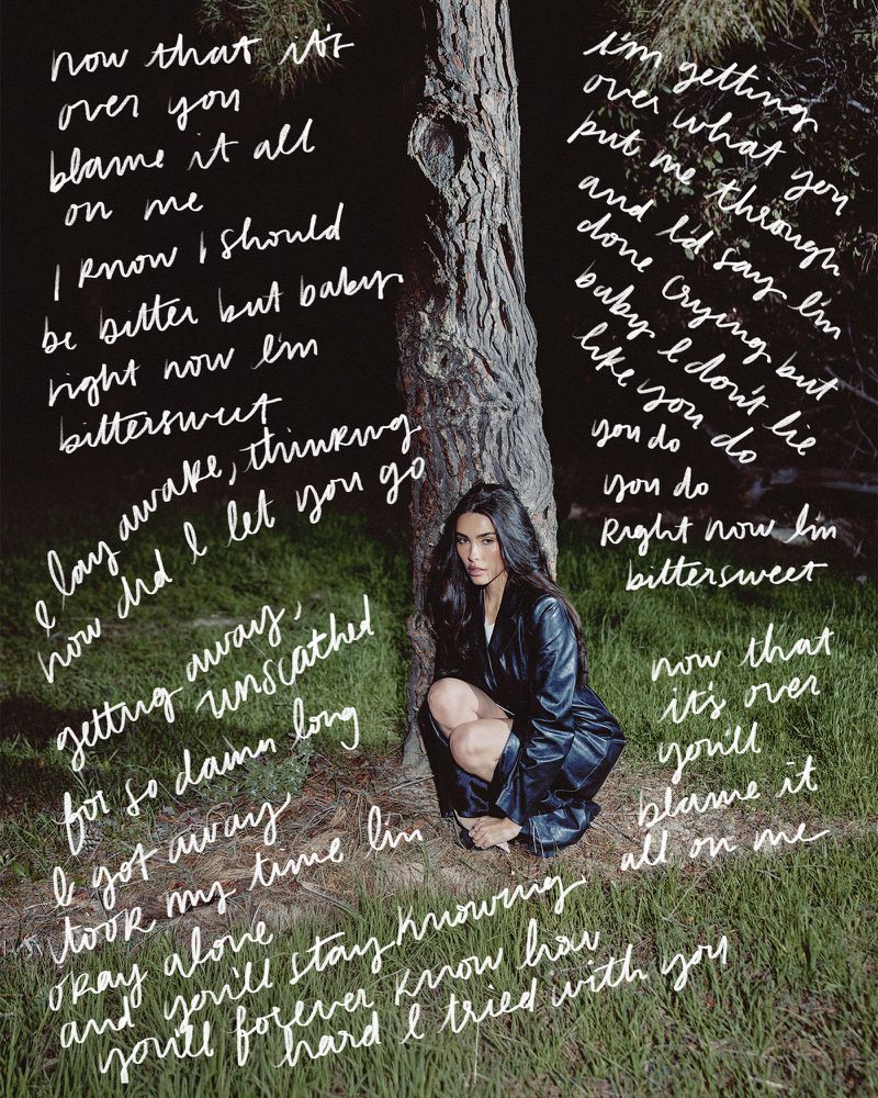 Madison Beer poses in a black leather jacket next to a tree, surrounded by handwritten lyrics on a grassy field in dim lighting.
