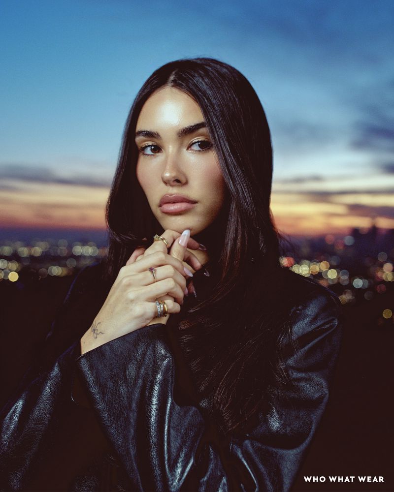 Madison Beer poses in a low-angle shot, wearing a black leather jacket against an atmospheric twilight backdrop, showcasing glossy lips.