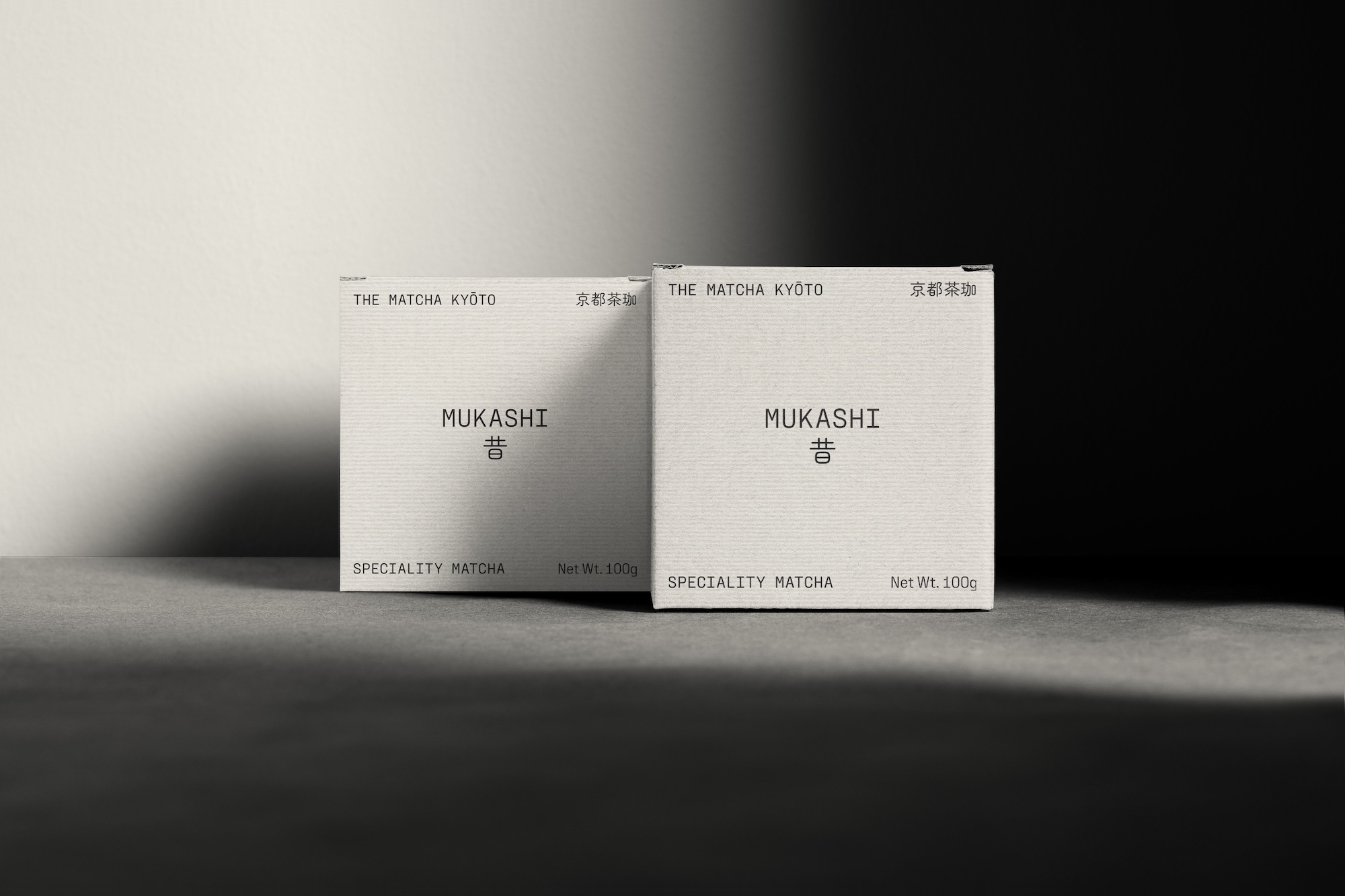Two Mukashi matcha tea boxes from The Matcha Kyoto, neatly arranged on a gray surface with distinct light and shadow interplay.