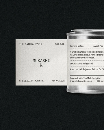 The Matcha Kyoto's Mukashi matcha product with its packaging featuring a label and a silver tin container, presented on a dark backdrop.