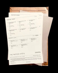 Printed paper menu sheets layered on top of textured cardboard packaging against a solid black background.