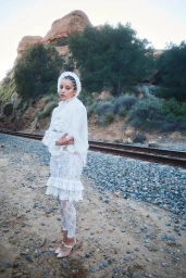 Chase Infiniti wearing a white lace dress and headpiece standing by railroad tracks for The Sunday Times Style Magazine UK