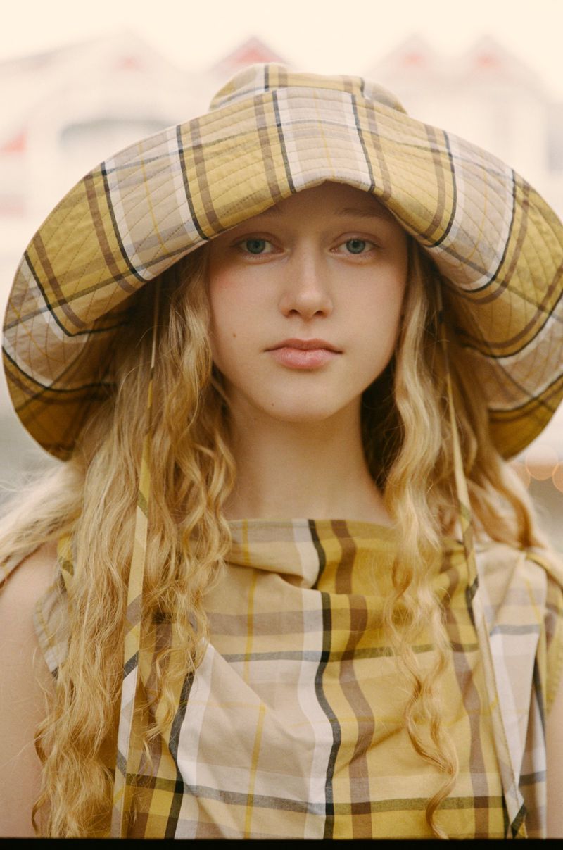 Portrait of a young woman with long blonde hair and a plaid hat and matching top, captured in natural outdoor lighting.