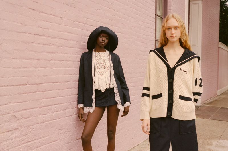Two women in fashionable nautical-themed clothing pose outdoors against a pink brick wall in natural light. Fashion editorial shot.