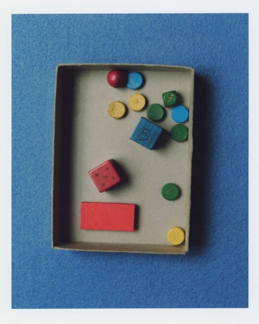 A cardboard box containing an assortment of colourful wooden blocks, circles, and other shapes arranged against a blue background.
