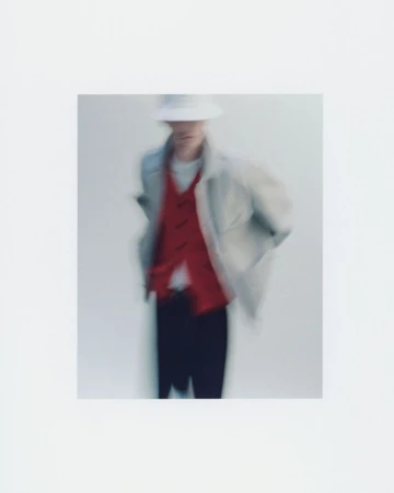 Motion blurred fashion portrait of a male model wearing a red vest and light jacket against a white background.