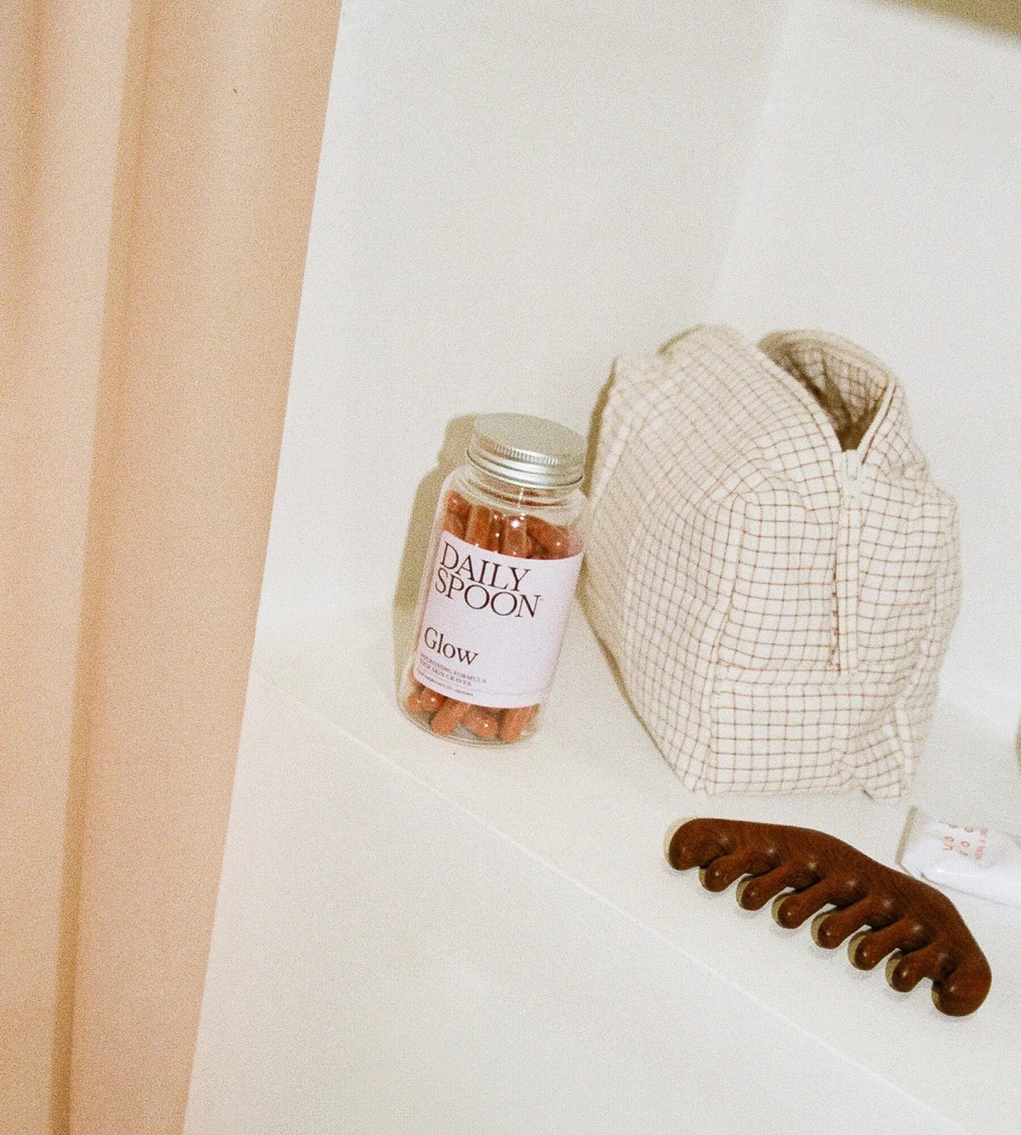 Cosmetic bag with vitamins and a hair comb on a white surface. Bottle of vitamins with the Daily Spoon logo.