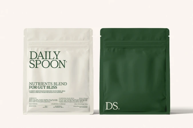 Two sealed Daily Spoon nutrient blend packages, one white and one dark green, stand side-by-side against a pale neutral background.