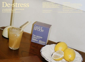 De-stress supplement box by Daily Spoon beside a glass of juice and fresh lemons on a wooden surface