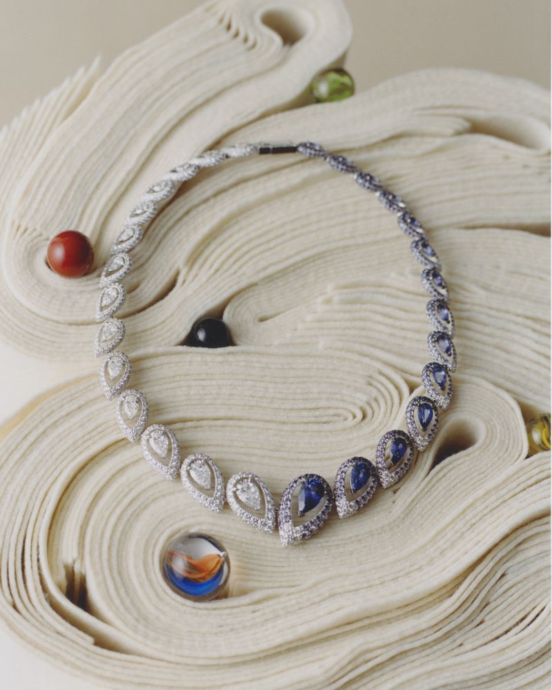Elegant necklace featuring a gradient of white to blue teardrop gemstones, displayed on a curled paper background, evokes luxury jewelry.