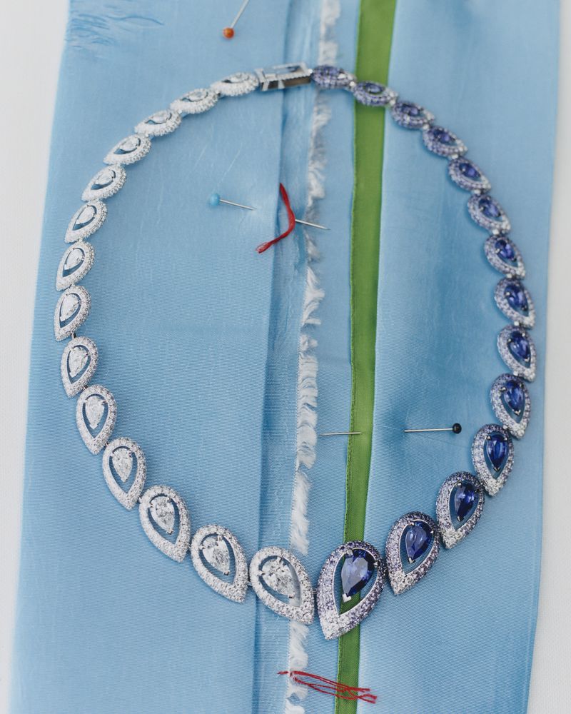 Elegant white gold necklace with teardrop sapphire and diamond pendants is pinned to light blue fabric, capturing fashion jewelry design.