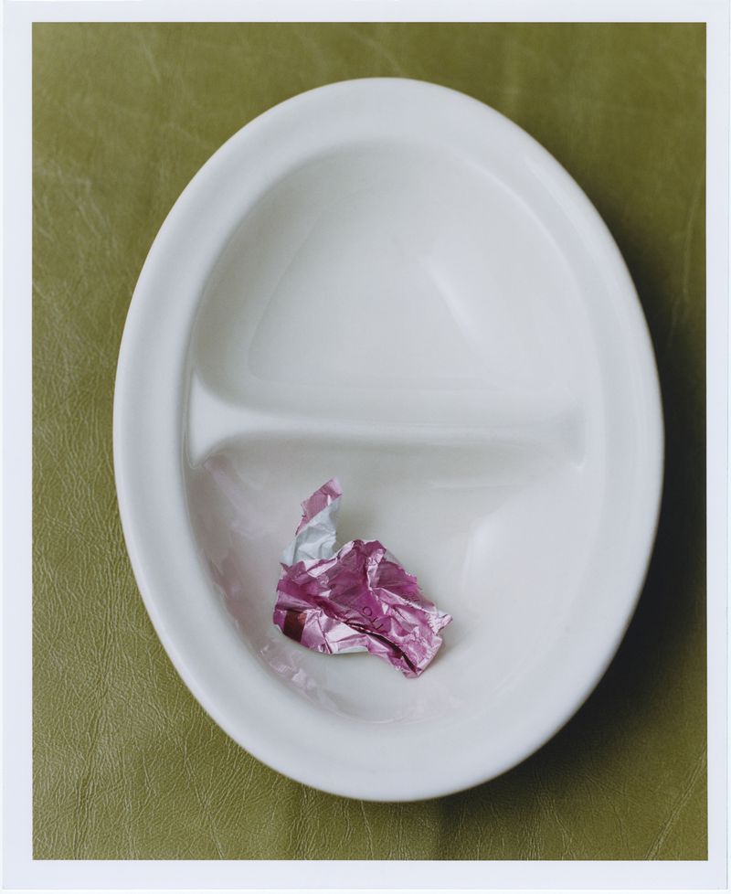 White divided plate on a light green surface featuring a small crumpled piece of pink foil in one section, studio lighting.