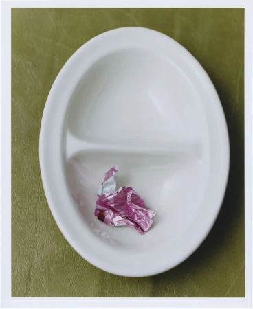 White divided plate on a light green surface featuring a small crumpled piece of pink foil in one section, studio lighting.