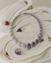 Diamond and sapphire necklace resting on folded cream paper sculpture with colorful glass beads