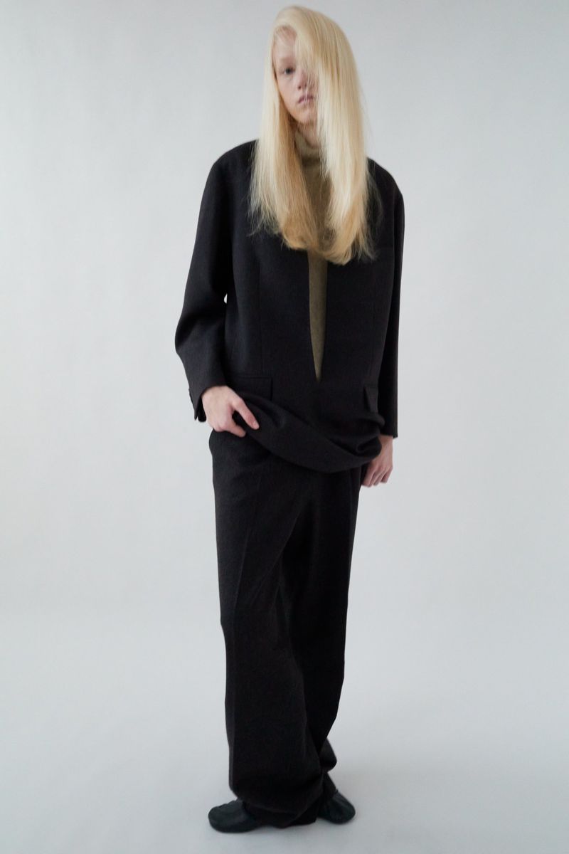 Full-length studio portrait of a blond adult female wearing a black blazer, pants, and shoes, against a neutral white background.