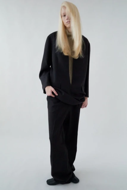 Full-length studio portrait of a blond adult female wearing a black blazer, pants, and shoes, against a neutral white background.
