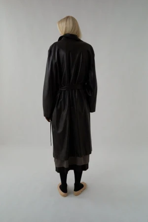 Model seen from behind wearing a dark leather belted coat against a plain white studio background.