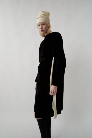 Model wearing a dark velvet dress and light beige draped headwrap against a plain white background