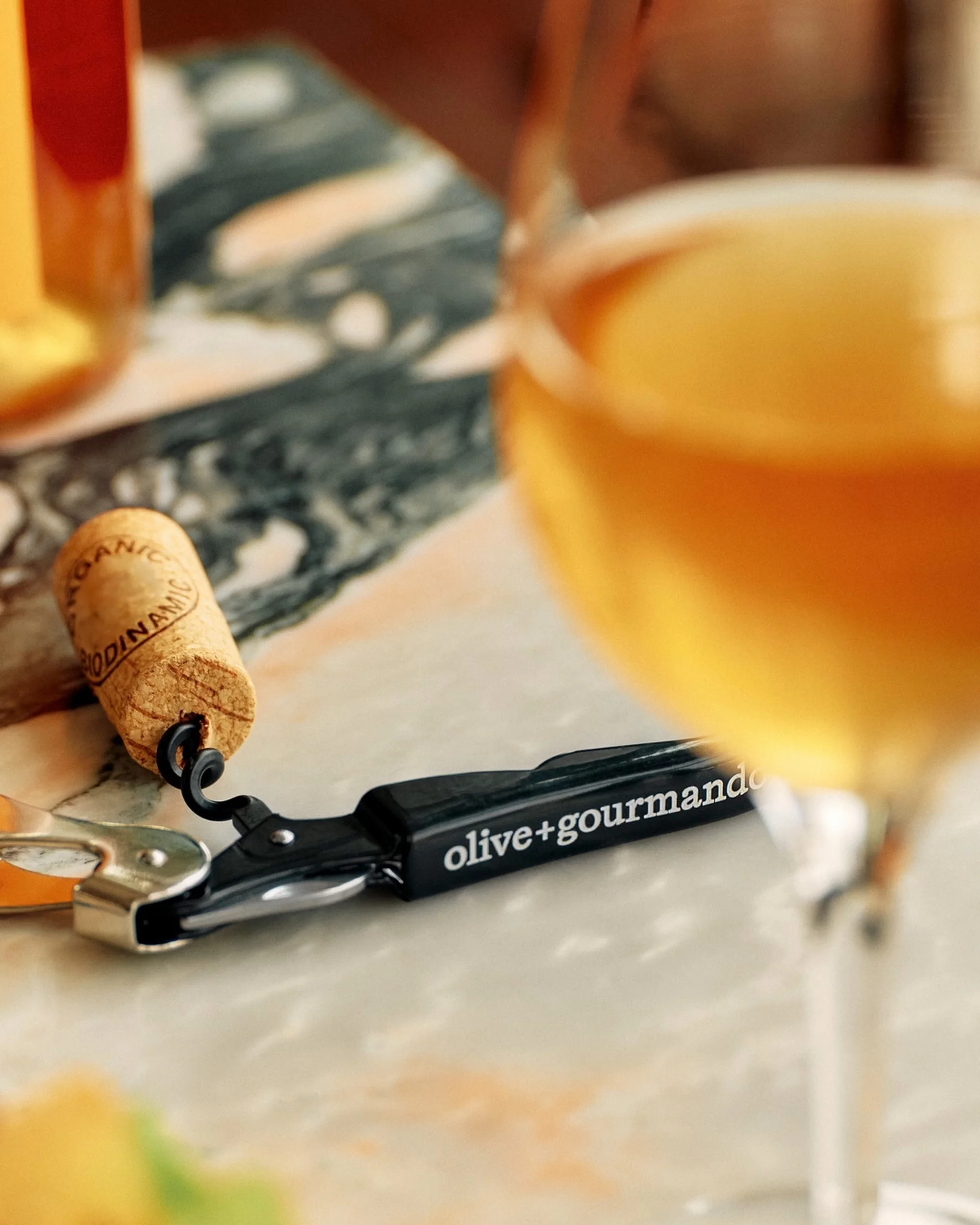 Close-up still life of a wine glass with white wine, cork, and corkscrew on a marble surface, creating a refined and inviting composition.