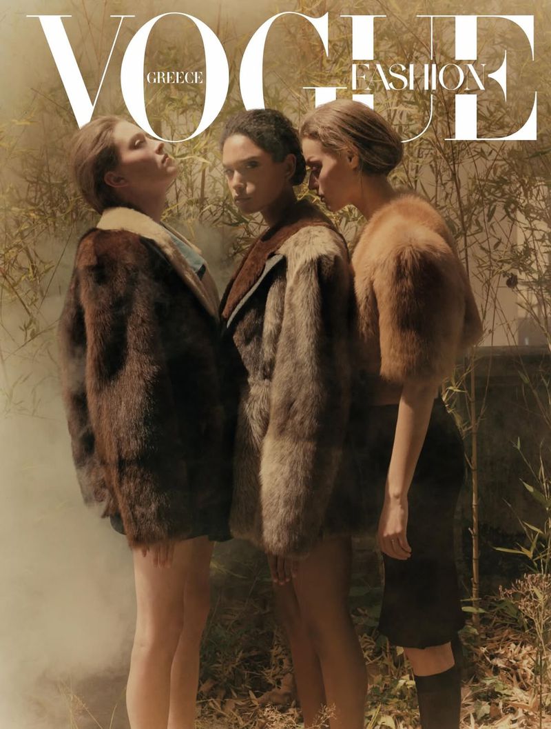 Vogue Greece cover featuring three female models in fur coats standing in a foggy outdoor environment with foliage in the background.