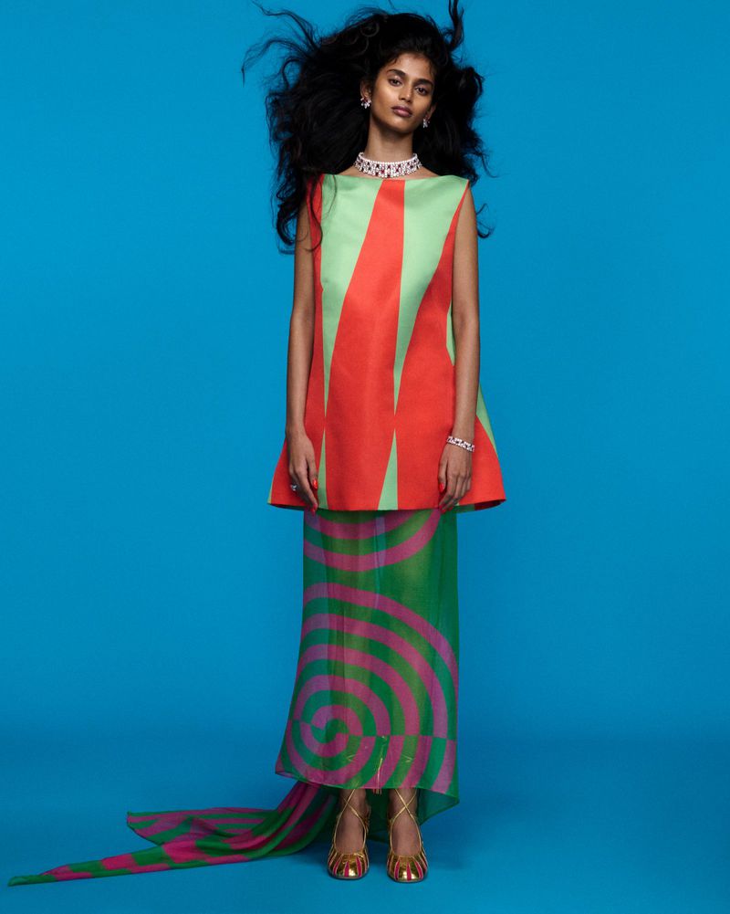 Elegant South Asian woman in a geometric-patterned sleeveless top and long skirt with a train posing in a blue photo studio.