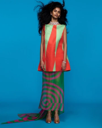 Elegant South Asian woman in a geometric-patterned sleeveless top and long skirt with a train posing in a blue photo studio.
