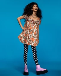 Model in floral minidress and polka dot leggings against a bright blue background