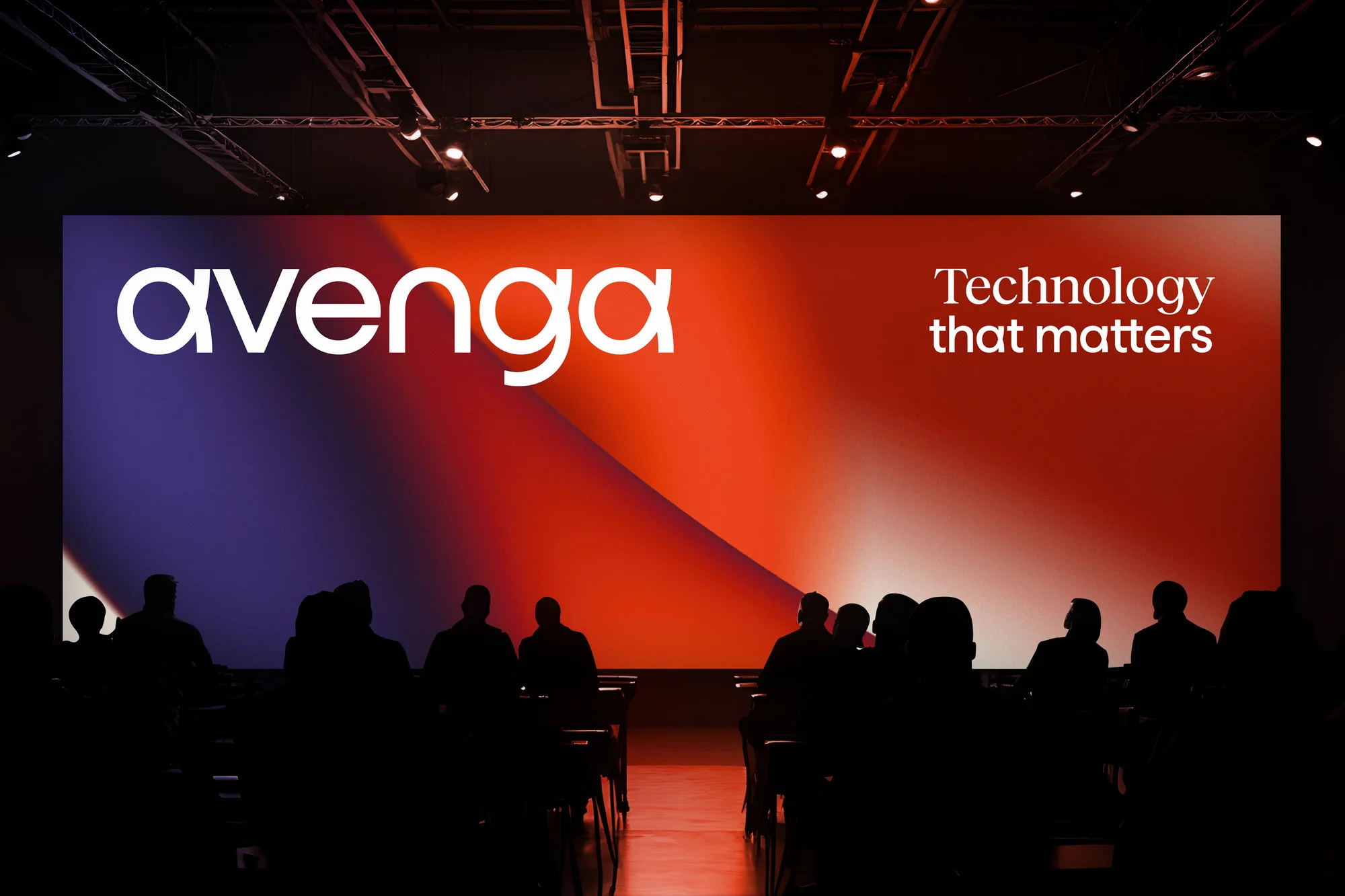 Audience silhouettes watch 'Avenga' presentation on a vibrant orange and purple stage, enhancing the technology showcase atmosphere.