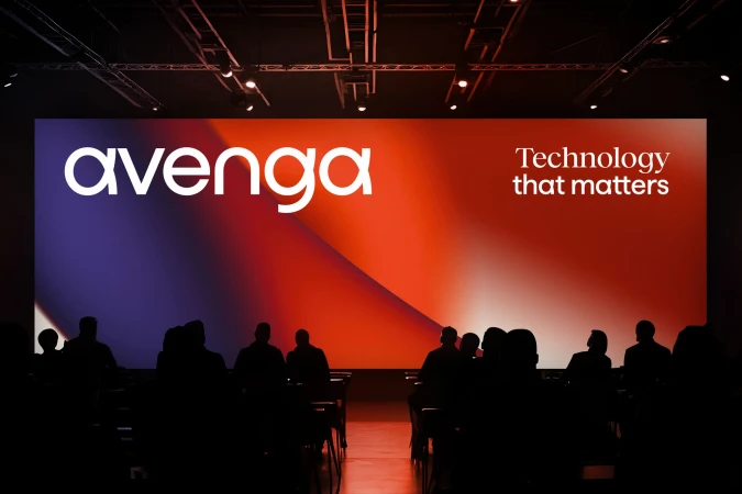 Audience silhouettes watch 'Avenga' presentation on a vibrant orange and purple stage, enhancing the technology showcase atmosphere.