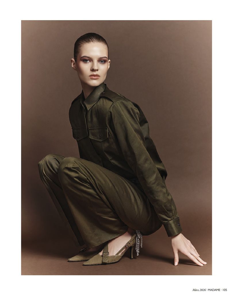Model in olive green shirt and trousers crouching against a brown studio backdrop for Madame Germany Safari Couture.