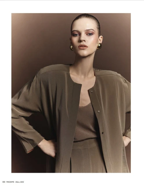 Fashion editorial shot of a female model with slicked-back hair wearing an olive-green outfit with large gold earrings in a studio.