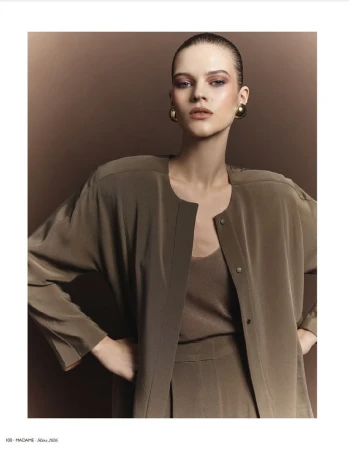 Fashion editorial shot of a female model with slicked-back hair wearing an olive-green outfit with large gold earrings in a studio.