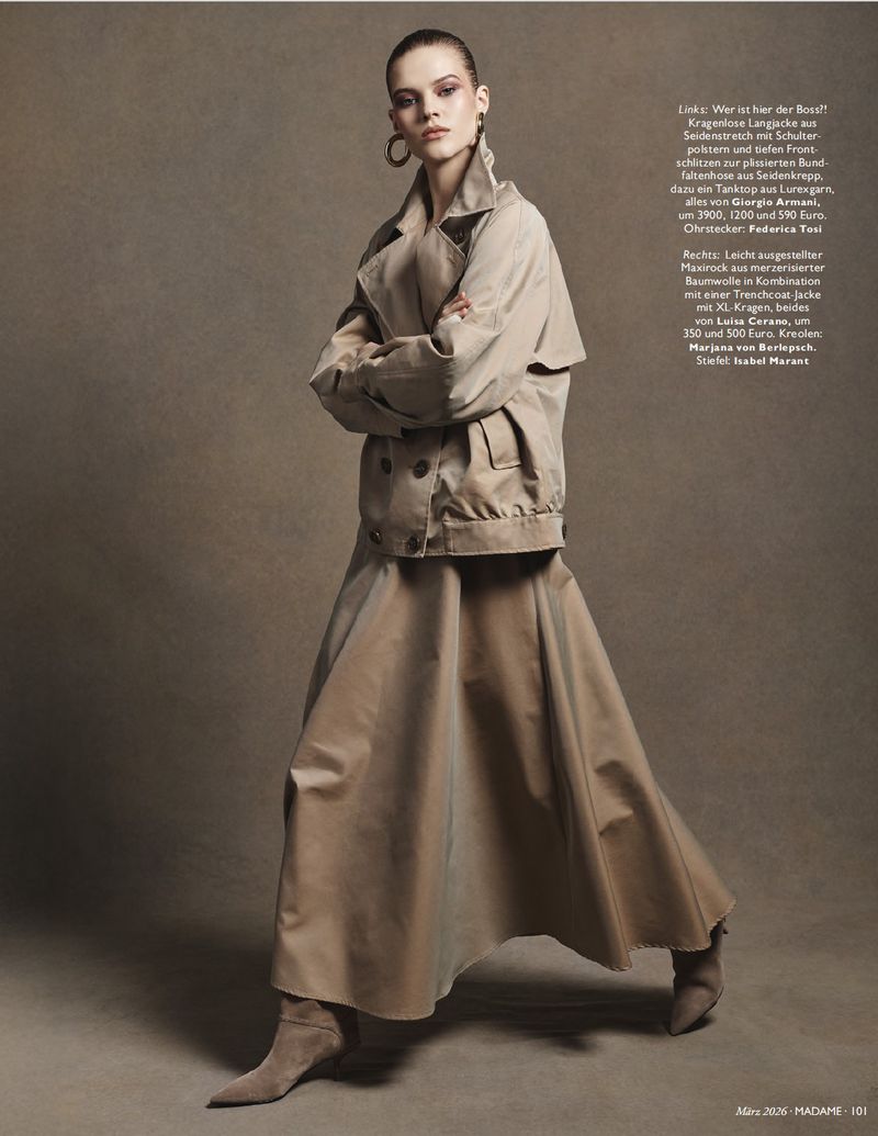 Fashion shot of a woman in a trench coat and maxi skirt. Model poses in an indoor studio setting with neutral background and soft lighting.