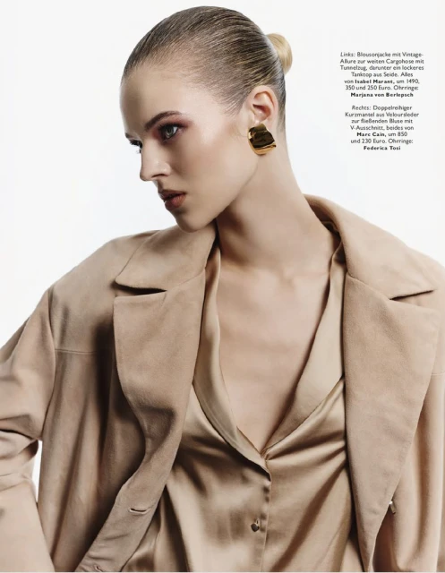 Fashion editorial shot of a woman in a neutral-toned satin shirt and suede jacket, posing in a studio against a white background.